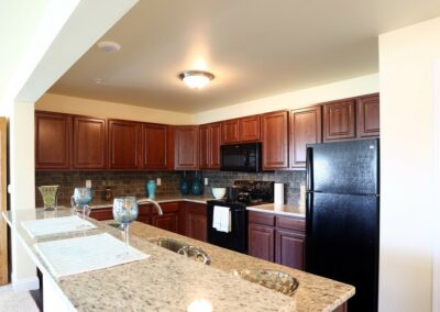 View of kitchen at The Reserve at Manada Hill in Hershey PA. Red wood stained cabinets, black kitchen appliances, granite counter tops. Hershey Apartments for Rent